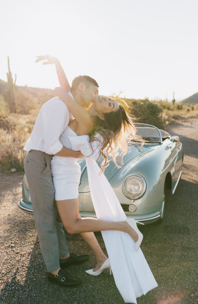 J and Alice's Blue Classic Car Arizona sunrise Engagement Session. J & A standing in front of the blue classic car sharing a passionate embrace