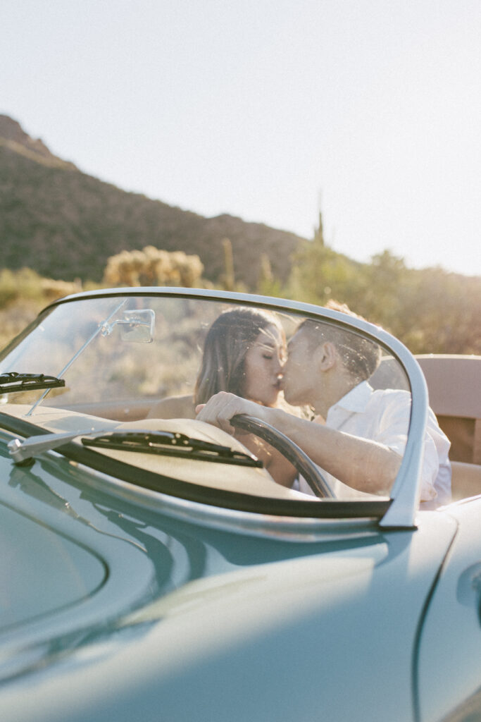 J and Alice's Blue Classic Car Arizona Engagement Session. J & A standing outside of the blue classic car sharing a gentle kiss in the front seat