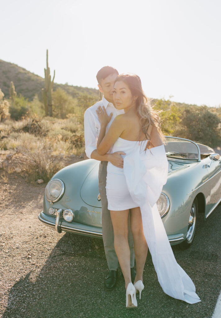 J and Alice's Arizona Sunrise Engagement Session sharing an embrace in front of the classic car, A looking over her shoulder