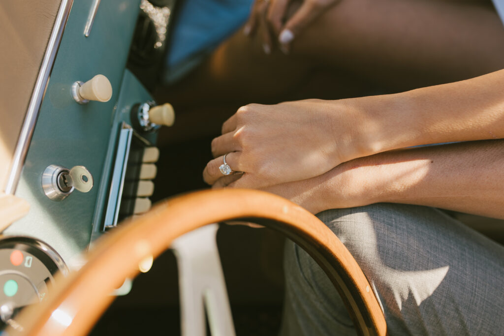 J and Alice holding hands in the front seat of the classic car capturing a close up of her ring during their Arizona Sunrise Engagement Session