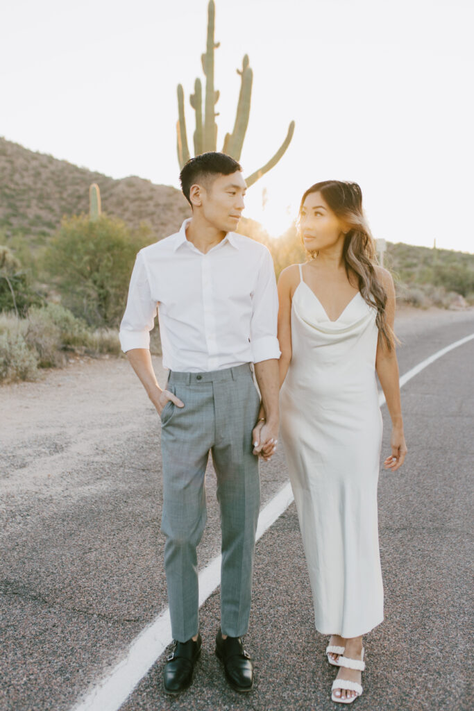 J and Alice’s Arizona Engagement Session walking hand in hand down the street away toward camera, looking at each other