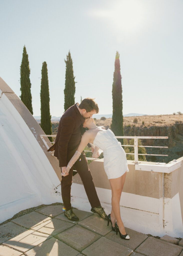 Bride and groom kiss on top of a structure at Arcosanti in the Arizona desert. 