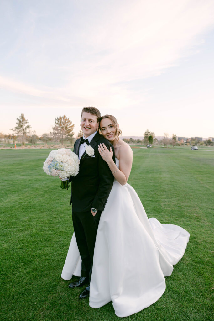 Bride and groom standing together on the golf course, smiling joyfully on their wedding day at the Arizona Biltmore Golf Club.