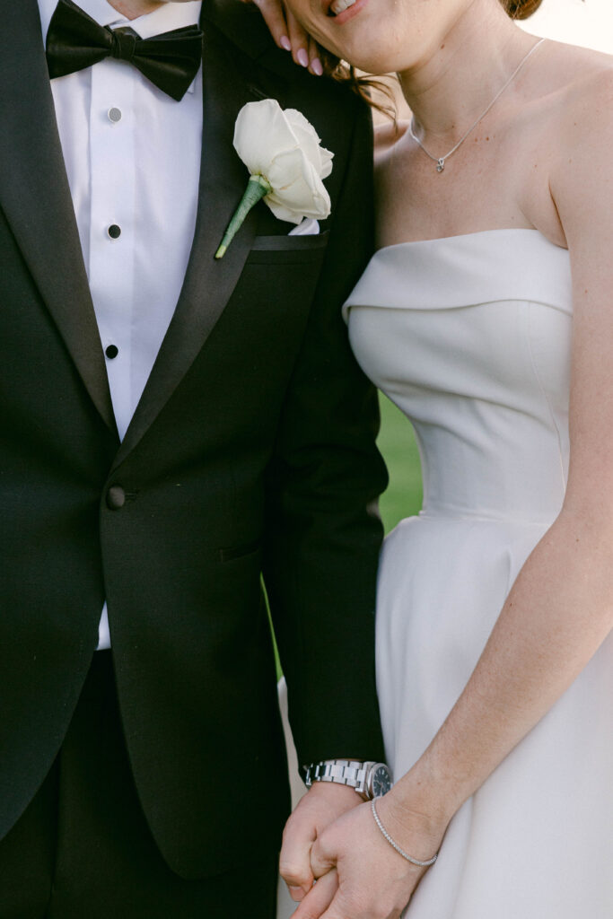 Close-up of bride and groom holding hands, showcasing elegant wedding attire and floral details.