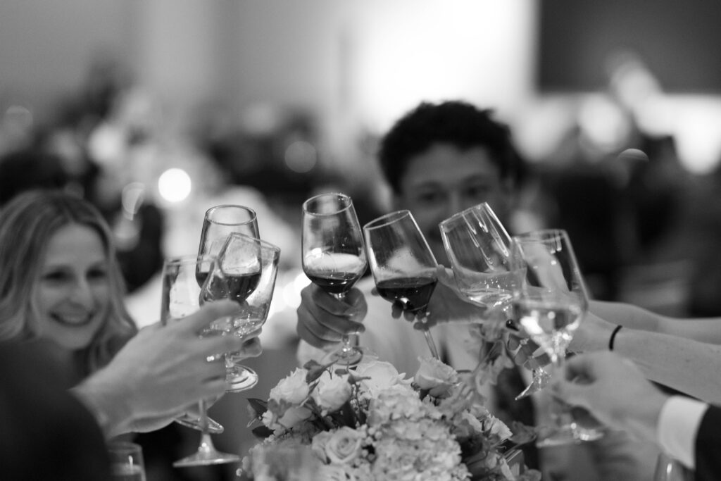 Wedding guests raising a glass in a heartfelt toast during the reception speeches, surrounded by candlelit tables and joyful smiles.