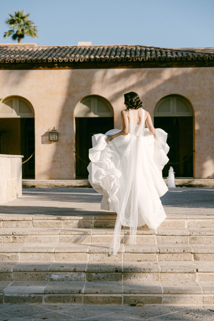 Beautiful bride in a flowy wedding dress posing gracefully at the Royal Palms Resort, surrounded by lush greenery and elegant architecture.