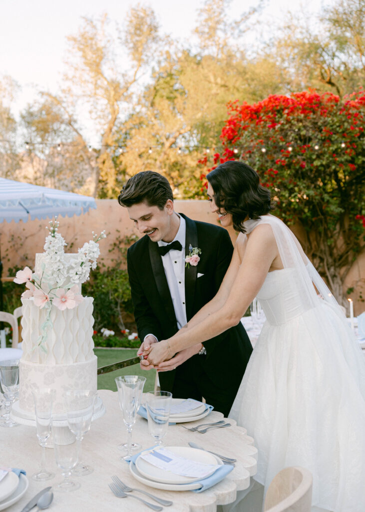 A newlywed couple sharing an intimate moment while cutting their wedding cake at Royal Palms Resort, surrounded by historic charm and lush greenery.