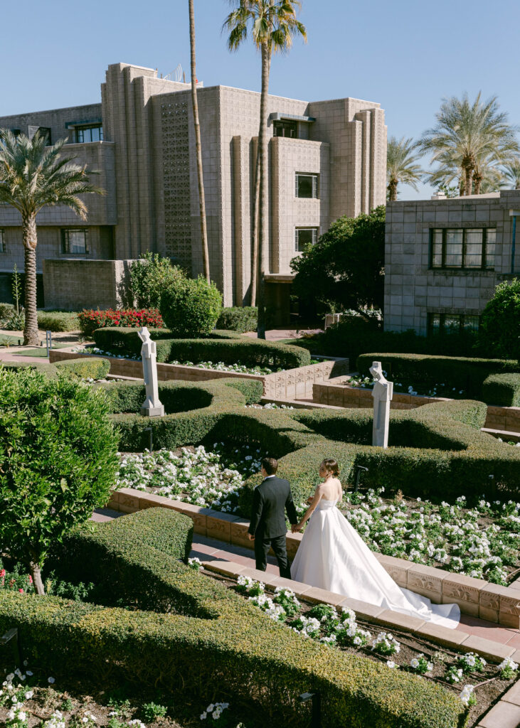 A romantic moment as a bride and groom stroll through the lush gardens of the Arizona Biltmore, surrounded by timeless architecture.