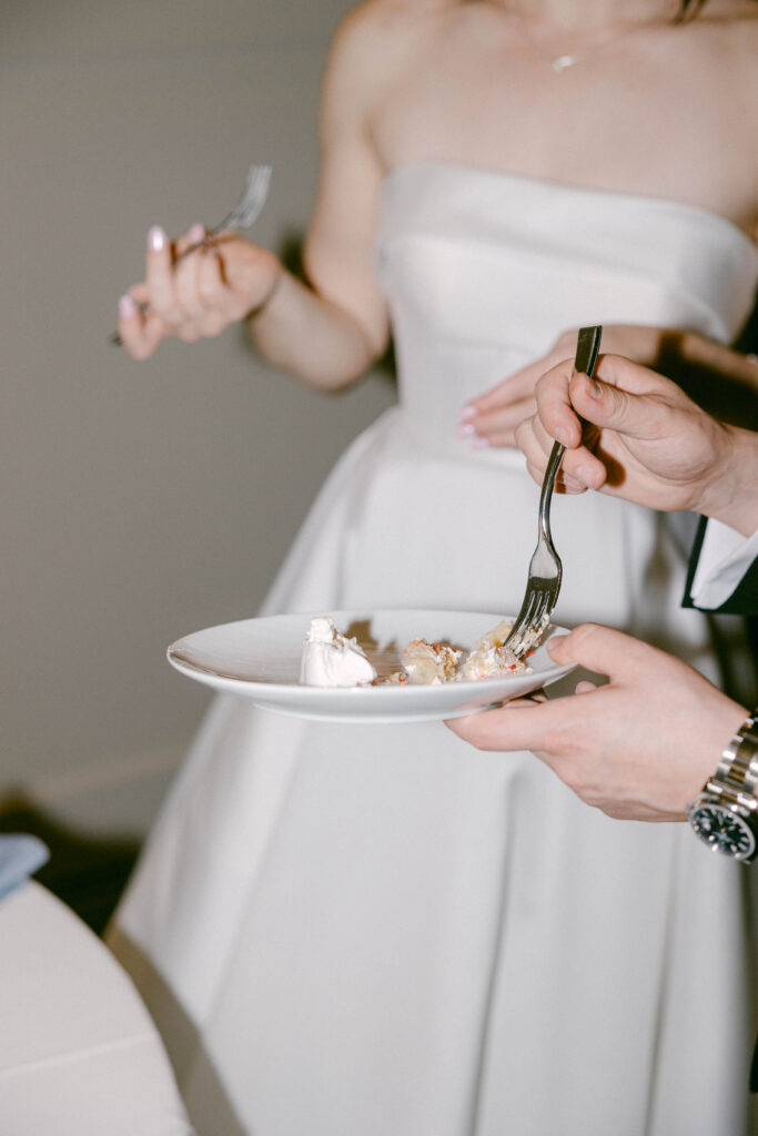 Bride and groom feeding each other a bite of their wedding cake after cutting it, capturing a sweet and intimate moment during their celebration.