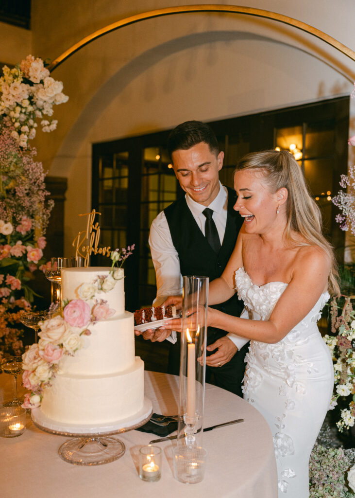 Bride and groom joyfully cutting their elegant wedding cake together, surrounded by romantic decor and a festive celebration.